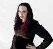 Summer on a plain white background wearing a black silk blouse, a black velvet waist cincher, and a necklace with red roses and thorns