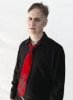 Roger on a plain white background wearing a black dress shirt with an open collar and a loose bright red necktie with a skeleton printed on the bottom #2